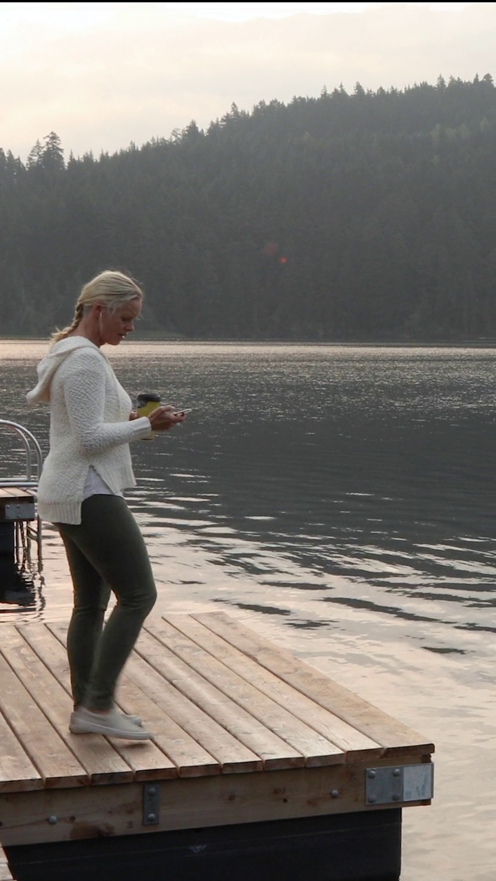 一个女人拿着饮料站在湖边的码头上视频下载
