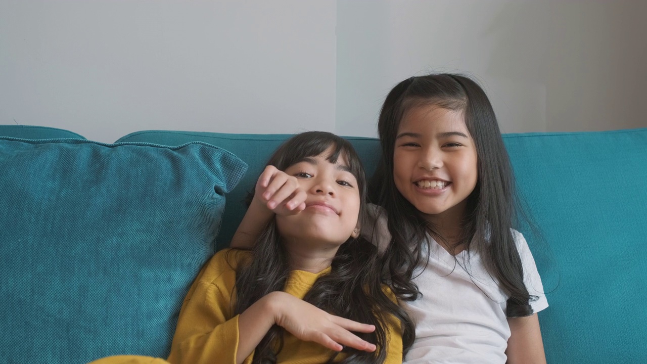 两个亚洲女孩是朋友微笑在沙发上。视频下载