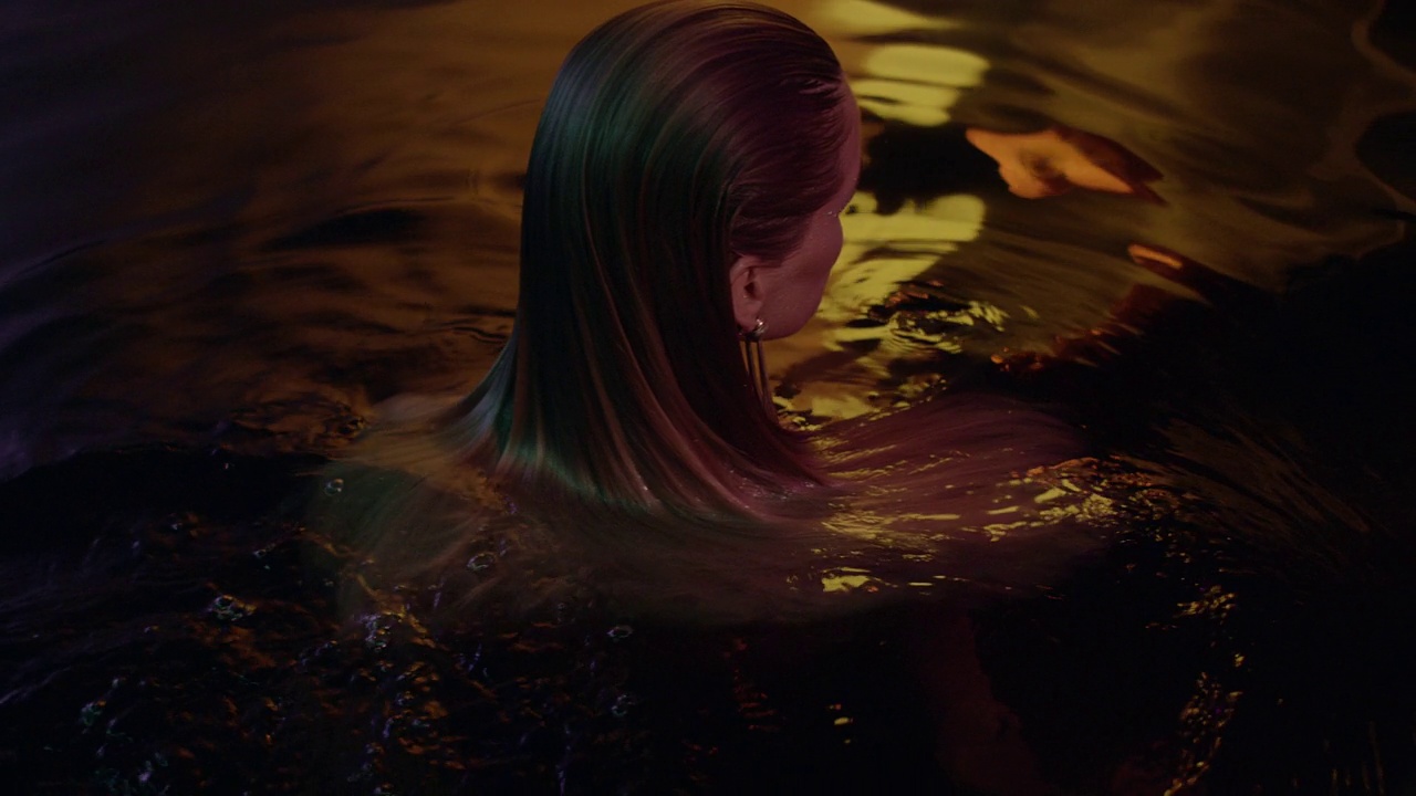 迷人的女人从深色、金色的水中浮现。关注长而健康的头发。视频素材