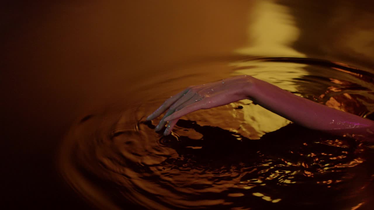 金色的，光滑的水面。女性用手轻轻泼洒并触摸液体视频下载