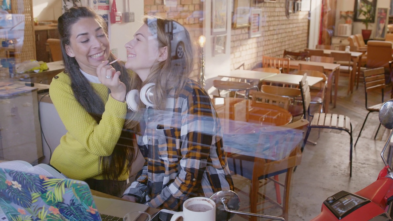 十几岁的女孩在咖啡馆的窗口给朋友涂唇彩视频下载