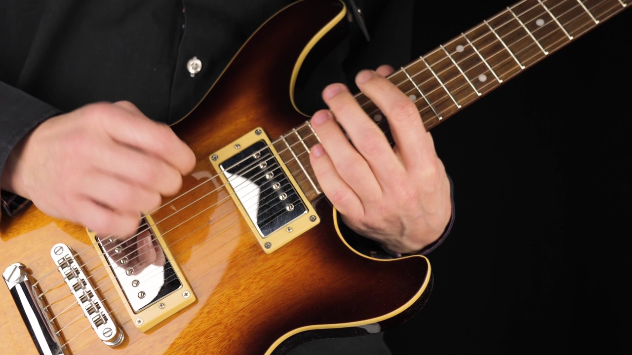 吉他手在黑色背景下弹奏浅棕色的六弦电吉他。在家做点音乐的概念。声音艺术的自由时间。中间。4 k视频素材