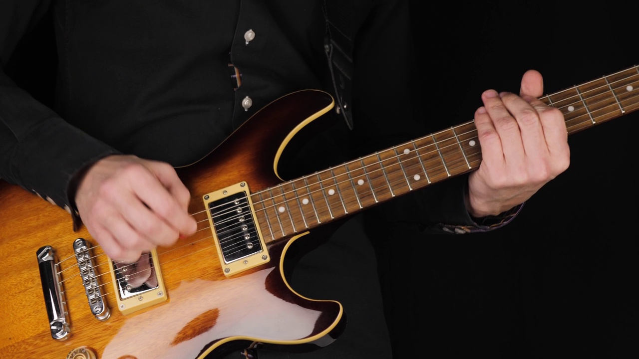 吉他手在黑色背景下弹奏浅棕色的六弦电吉他。在家做点音乐的概念。声音艺术的自由时间。广角镜头。4 k视频素材