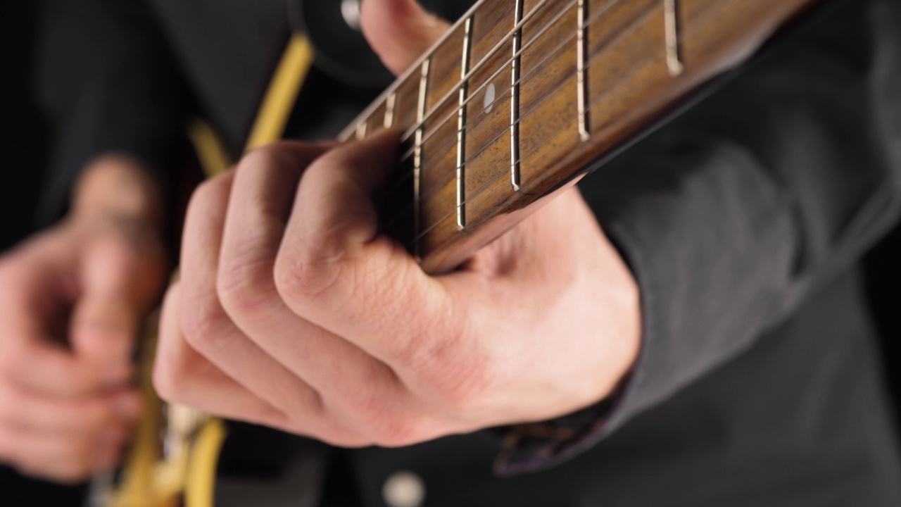 吉他手在黑色背景下弹奏浅棕色的六弦电吉他。在家做点音乐的概念。声音艺术的自由时间。关闭了。4 k视频素材