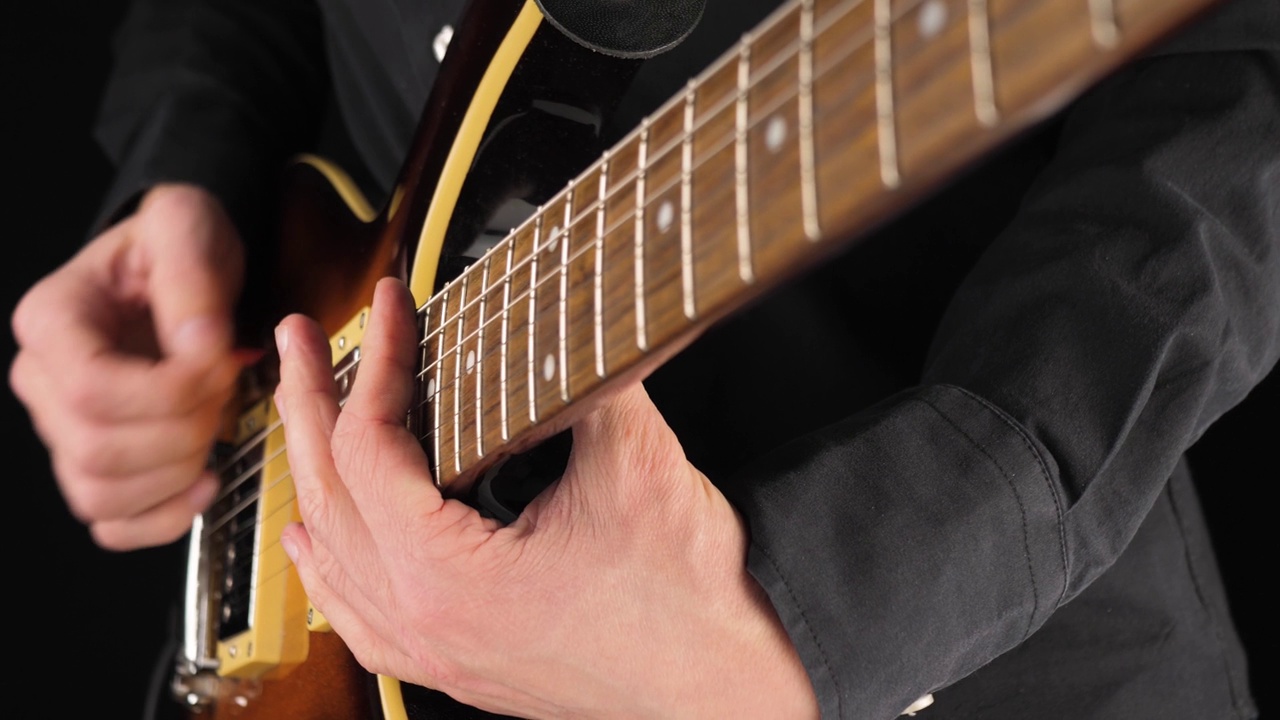 吉他手在黑色背景下弹奏浅棕色的六弦电吉他。在家做点音乐的概念。声音艺术的自由时间。关闭了。4 k视频素材
