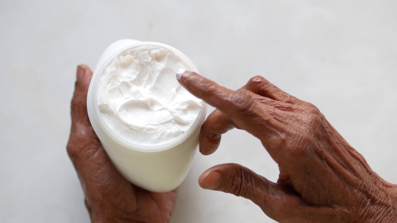 老年妇女在白色背景的皮肤上涂抹美容霜视频下载