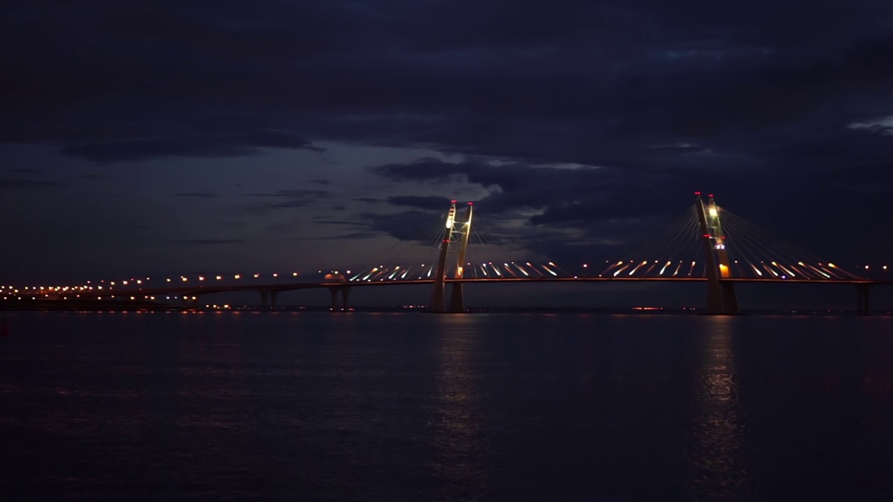 夜晚有灯光照亮的路的桥。镜头。大桥横跨城市岛屿之间的河流，飞鸟在镜框中飞翔，静观水面，平静如水视频下载