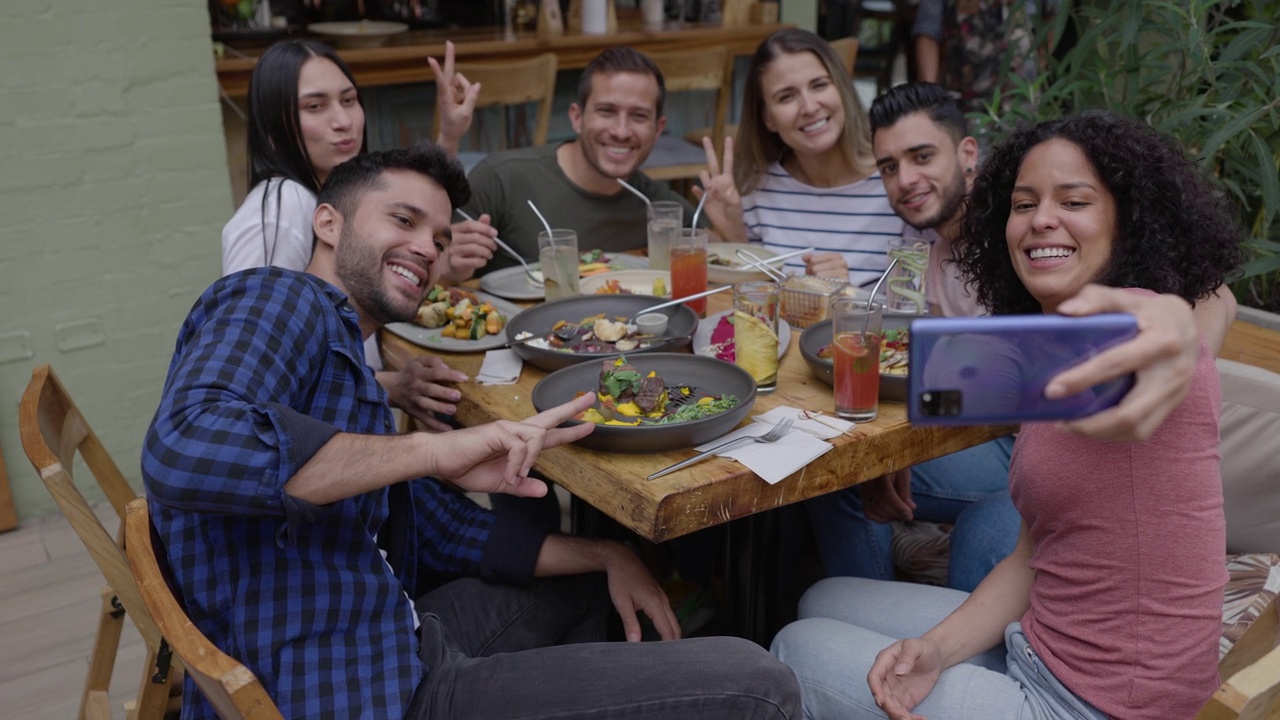 一群开心的朋友一边享受美味的饭菜一边自拍，他们都笑得很开心视频下载