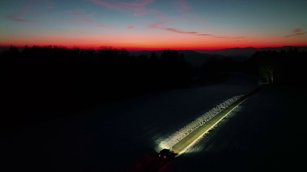 航拍:越野车行驶在雪山森林道路上，在令人惊叹的金色冬季日落股票视频视频下载