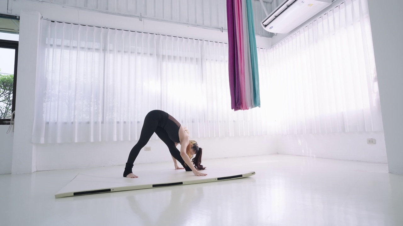 年轻的亚洲妇女示范瑜伽姿势在三角形。穿着黑色运动服的健身女性在健身室的白色床垫上做热身伸展运动，缓解肌肉紧张，增强柔韧性。年轻苗条的女孩做有氧运动。视频素材