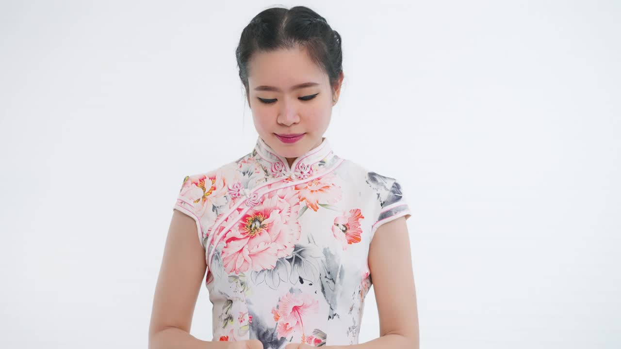 中国/亚洲妇女在春节期间打开红色购物袋迎接一个惊喜，白色的背景，穿着旗袍白色花卉图案的衣服视频下载