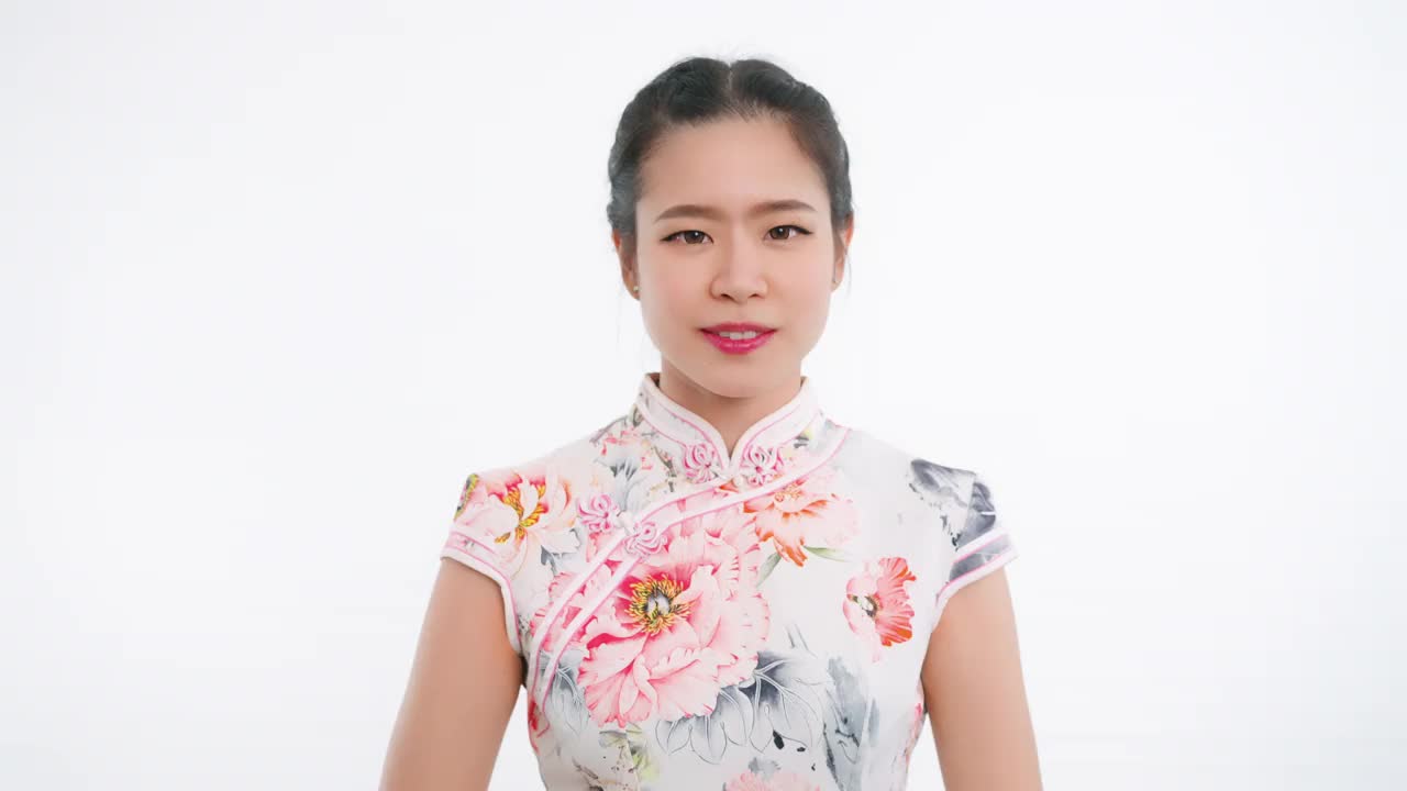 中国/亚洲妇女在春节期间，在白色的背景下，穿着旗袍，做着感谢的手势视频下载