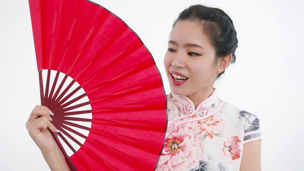 中国/亚洲美丽的女子在中国春节，拿着红色的扇子，微笑着看着镜头视频下载