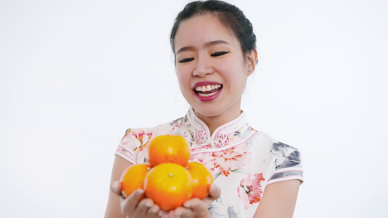 中国/亚洲妇女穿着旗袍，手持橘子，向镜头传递给家人、亲戚和朋友，表示新年快乐、富裕、幸福和幸运视频下载