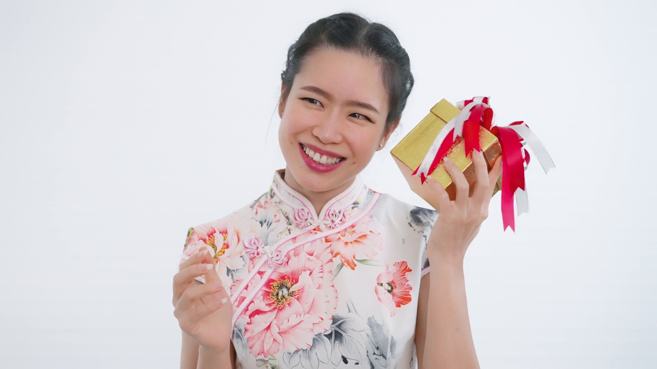 中国/亚洲妇女打开她手中的一个金色的大礼盒，她从她的家人，亲戚和朋友为新年的快乐，在中国的春节，穿着旗袍白色的衣服视频下载