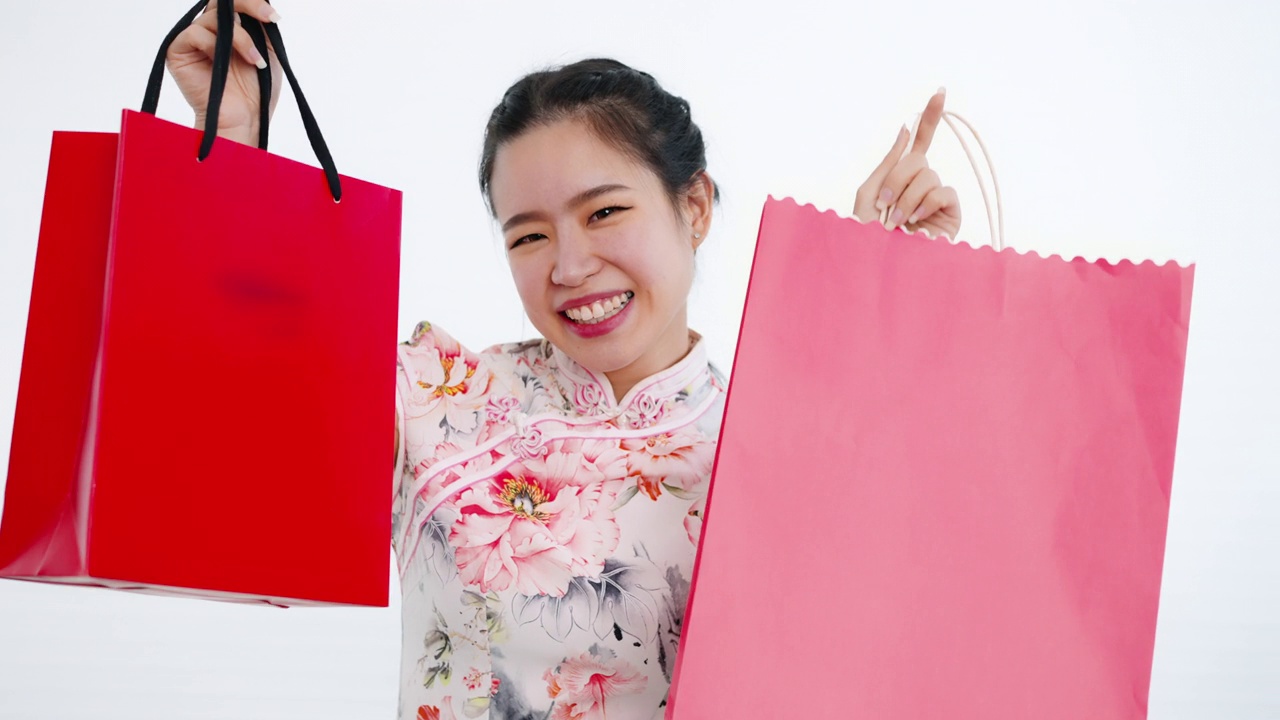 中国/亚洲妇女喜欢在春节期间带着红色购物袋去购物，白色的背景，穿着旗袍白色花卉图案的衣服视频下载