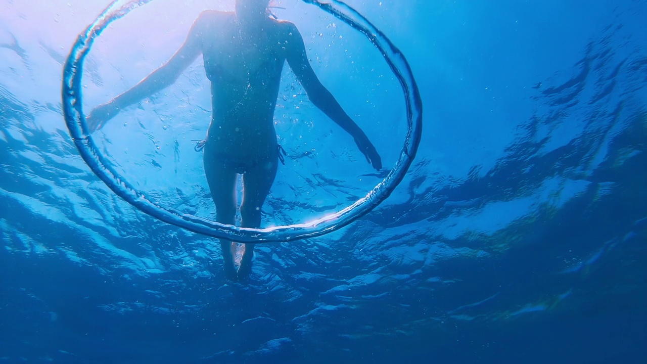 泡沫环。女子自由潜水者看着泡泡环在水下移动视频下载