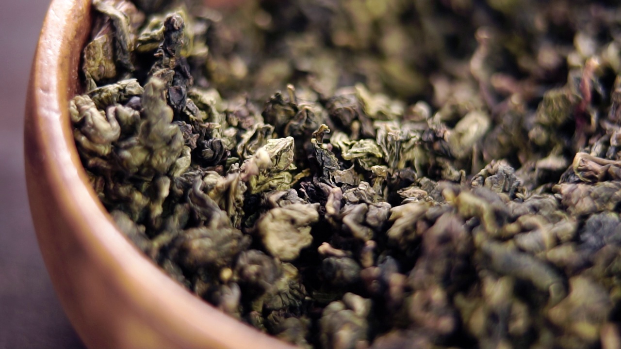 乡村木碗里的中国绿茶。手拿了一撮干树叶。以慢动作坠落视频下载