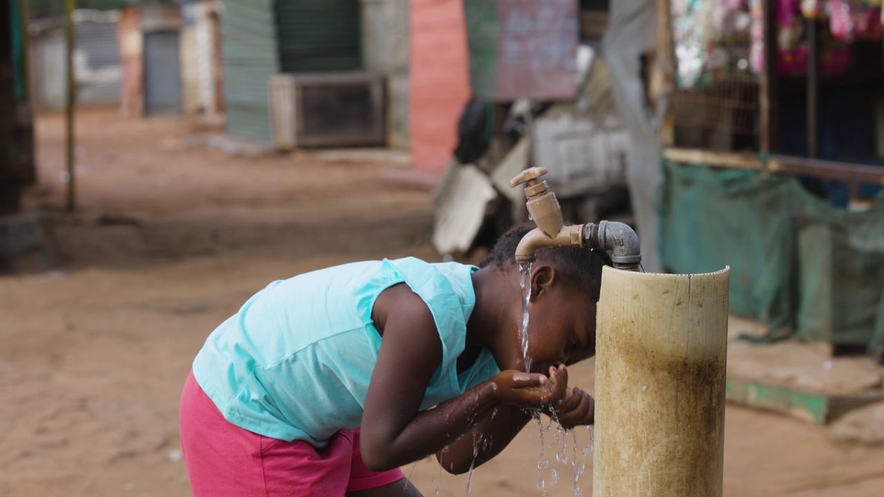 贫穷、不平等、贫穷的非洲黑人女孩在一个非正式的贫民窟里用公用水龙头喝水视频素材
