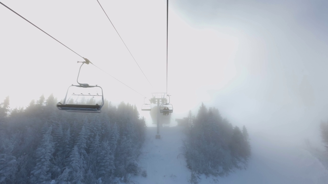 从滑雪椅升降机和雪炮喷洒人工雪在滑雪坡和树木的POV视频下载