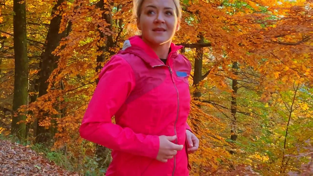 微笑的女人，享受大自然，在阳光明媚的秋天森林里跑步视频下载