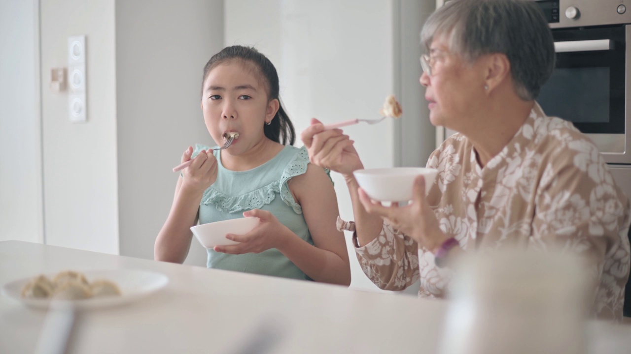 亚洲华裔孙女和她的祖母在厨房的柜台吃饺子视频下载