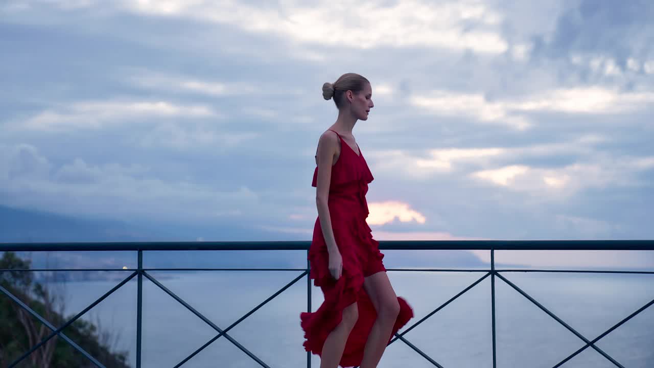 阳光明媚的露台上迷人的女人。穿着漂亮的红色连衣裙。用摄影机调情视频下载