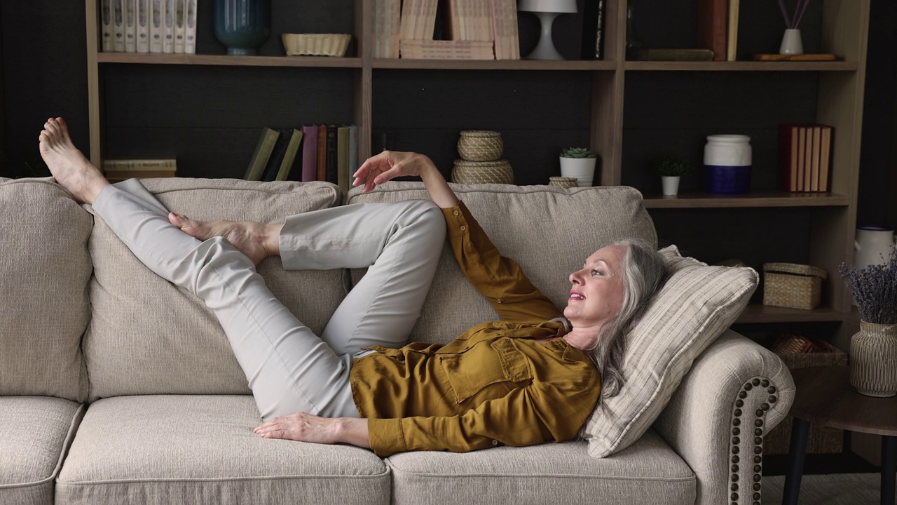 快乐的成年退休女性以舒适的姿势放松在沙发上视频素材