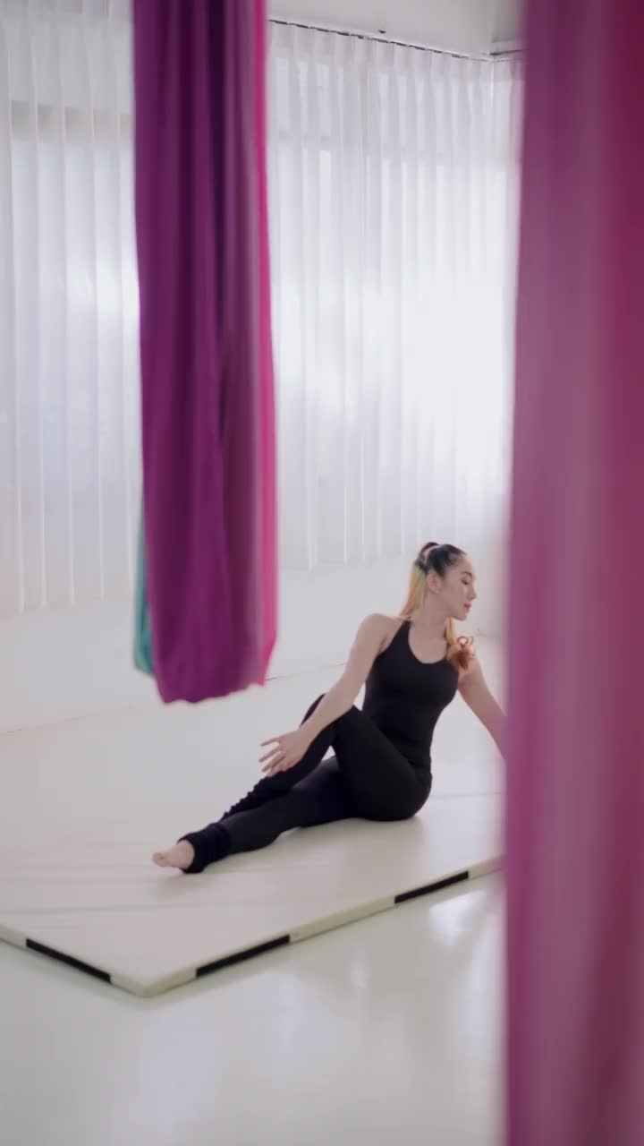 美丽的年轻亚洲女性穿着黑色运动服在瑜伽飞行课前热身，伸展，缓解肌肉紧张，在健身工作室的白色床垫上建立身体灵活性视频素材