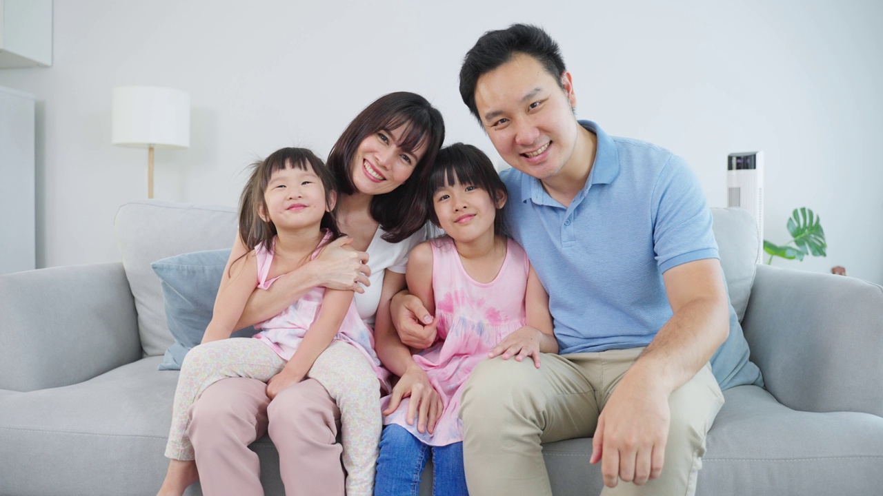 亚洲幸福家庭的肖像，花时间与孩子一起在家里。年轻可爱的小女孩和父母坐在沙发上微笑，看着客厅里的镜头。活动关系的概念视频素材
