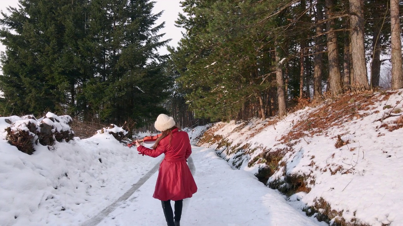 一个女人在冰冻的森林里的路上跳舞拉小提琴视频素材