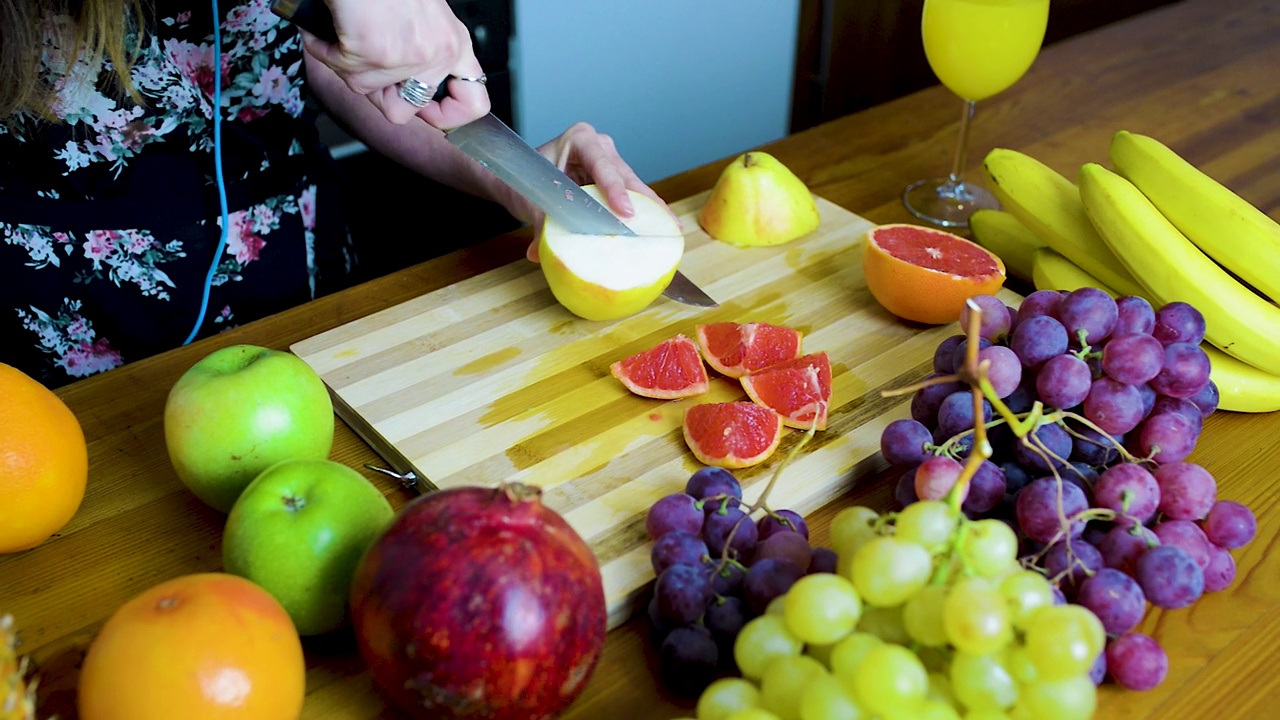 年轻女子用陶瓷刀在木砧板上切苹果。视频下载