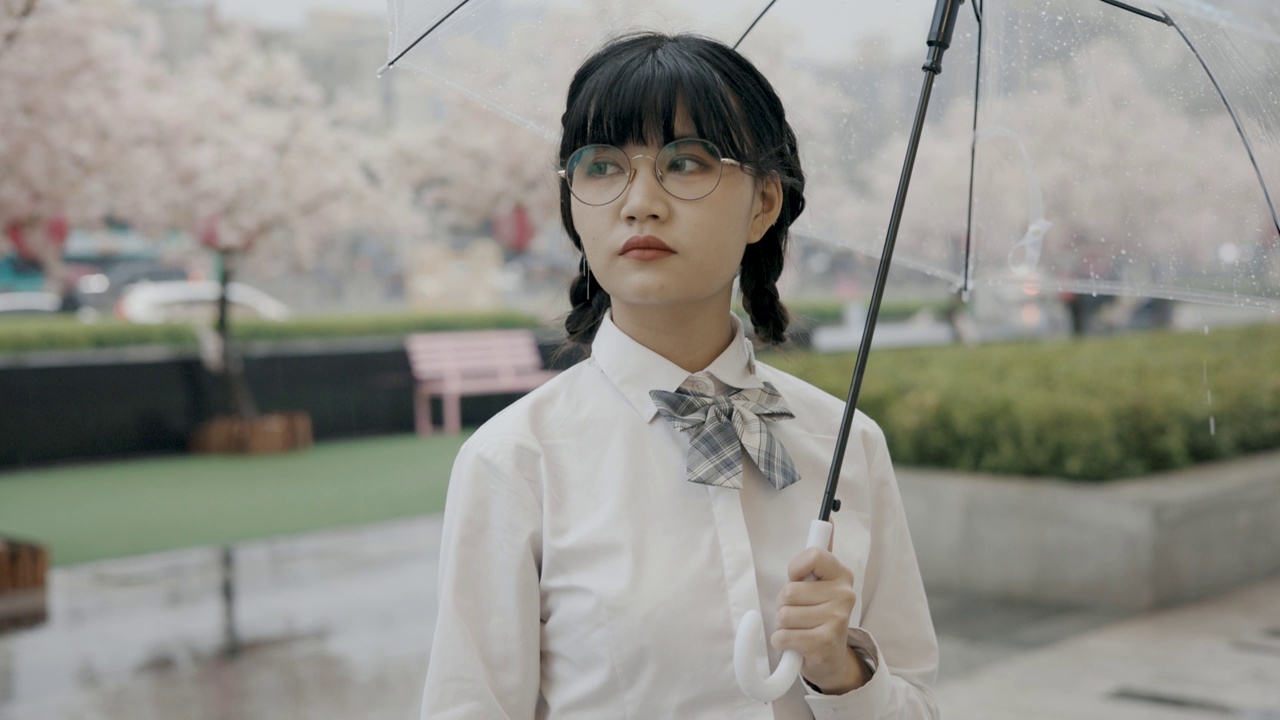 可爱的亚洲女生，穿着校服，打着伞，站在街上视频下载