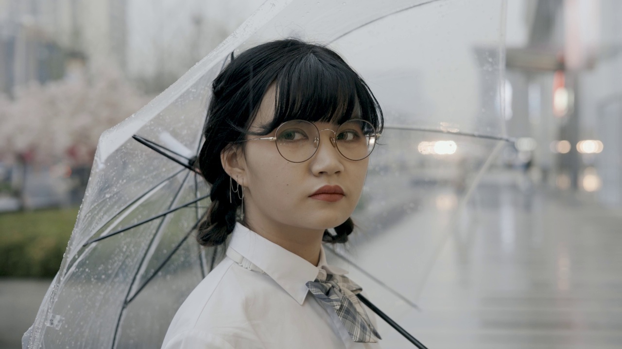 可爱的亚洲女生，穿着校服，打着伞，站在街上视频下载