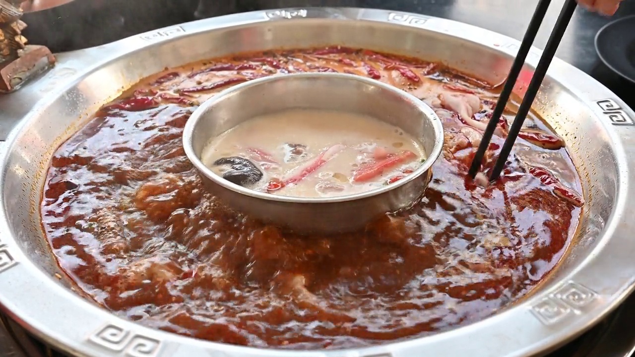 人们用筷子将肉放入辛辣的中国火锅的特写。视频下载