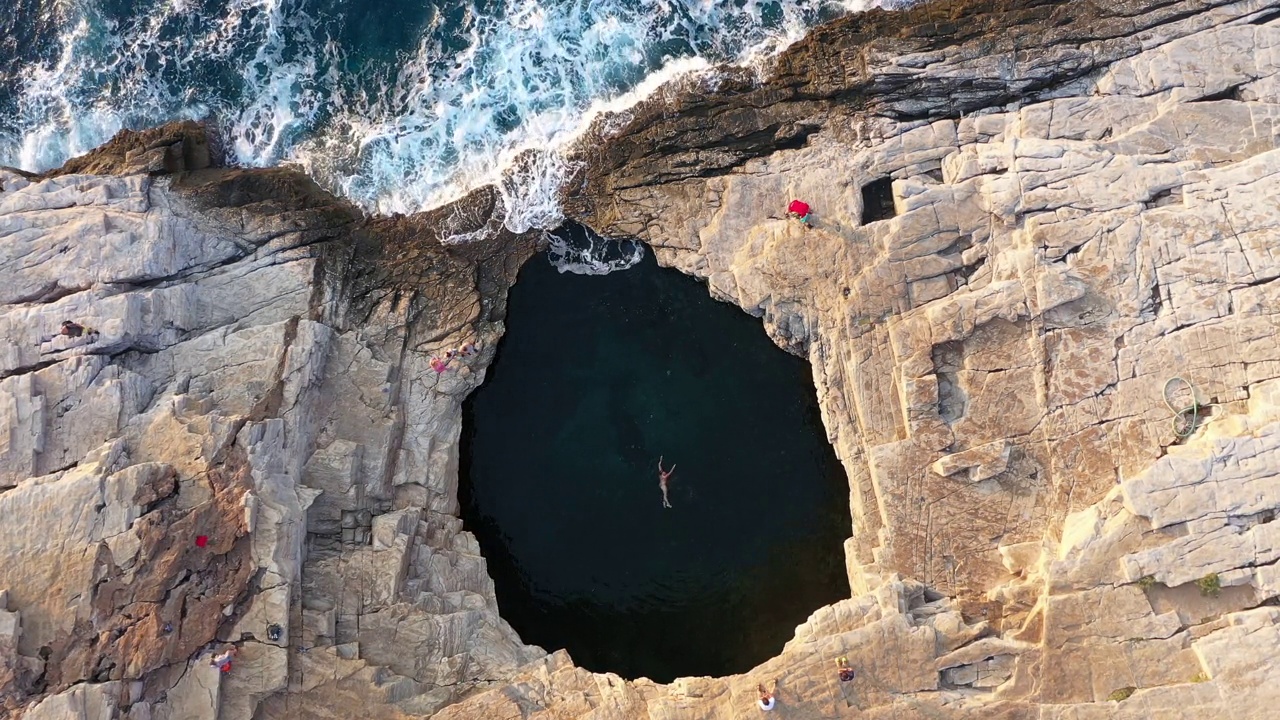 一名女子在岩石海岸的天然海水池中游泳。希腊塔索斯岛的吉奥拉泻湖，无人机拍摄视频下载
