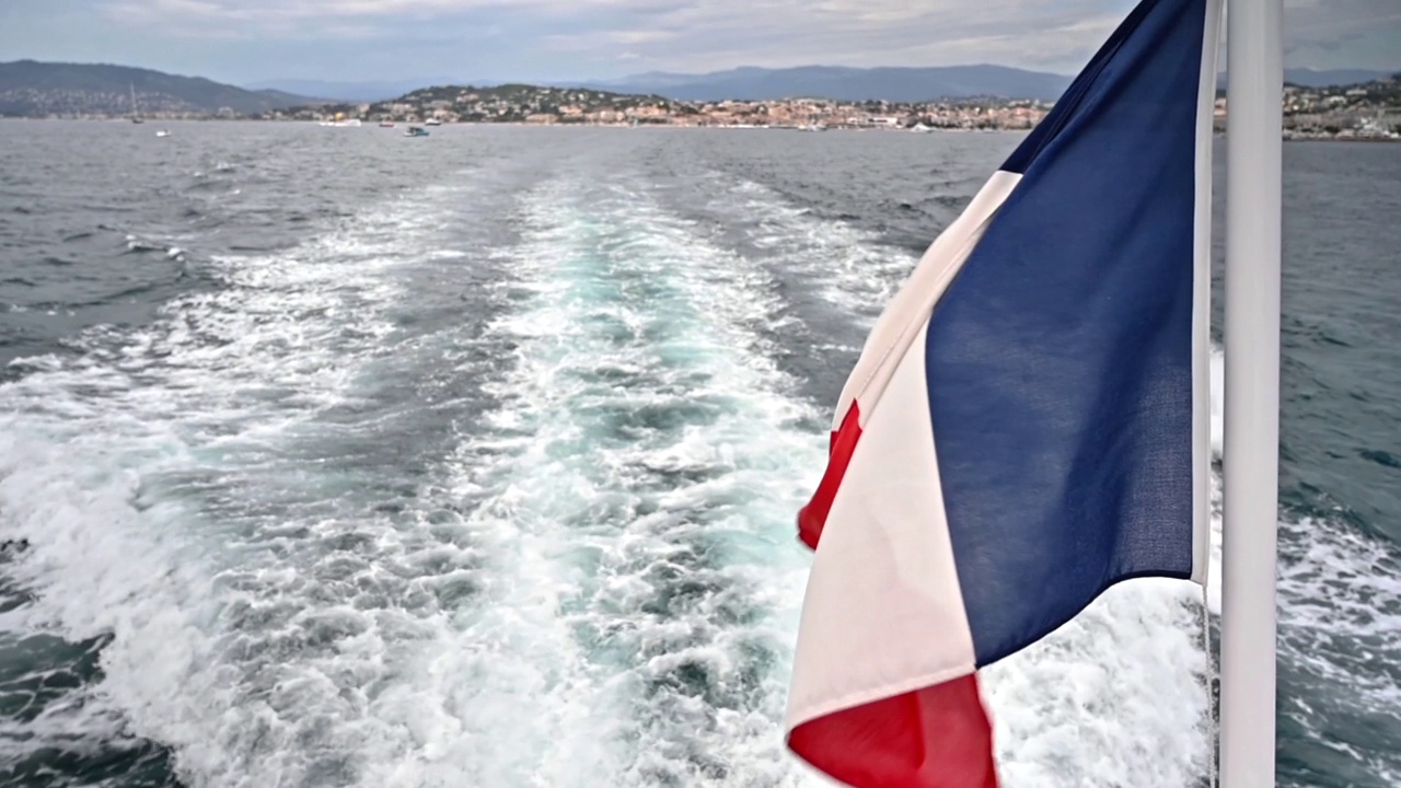 漂浮的小船上飘扬的法国国旗。远处是戛纳。法国。慢动作视频下载
