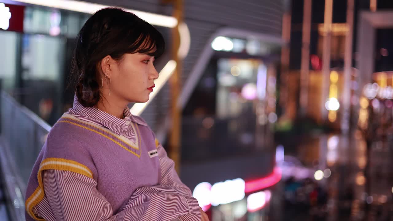 一幅年轻女子的肖像，在夜晚的城市霓虹灯的照耀下。视频素材
