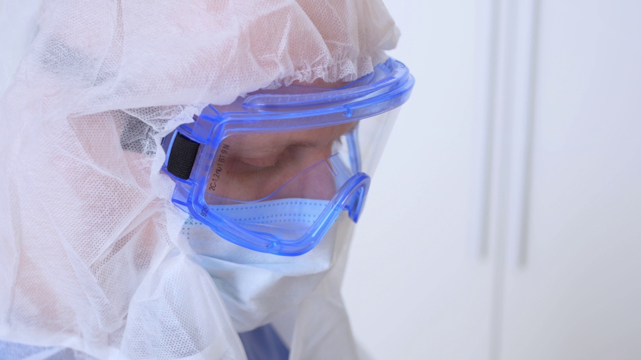 一个戴着护目镜和面罩的医生的脸部特写。医务工作者穿着一次性洗衣和带口罩的护目镜，在感染区或手术前工作。Caronovirus视频素材