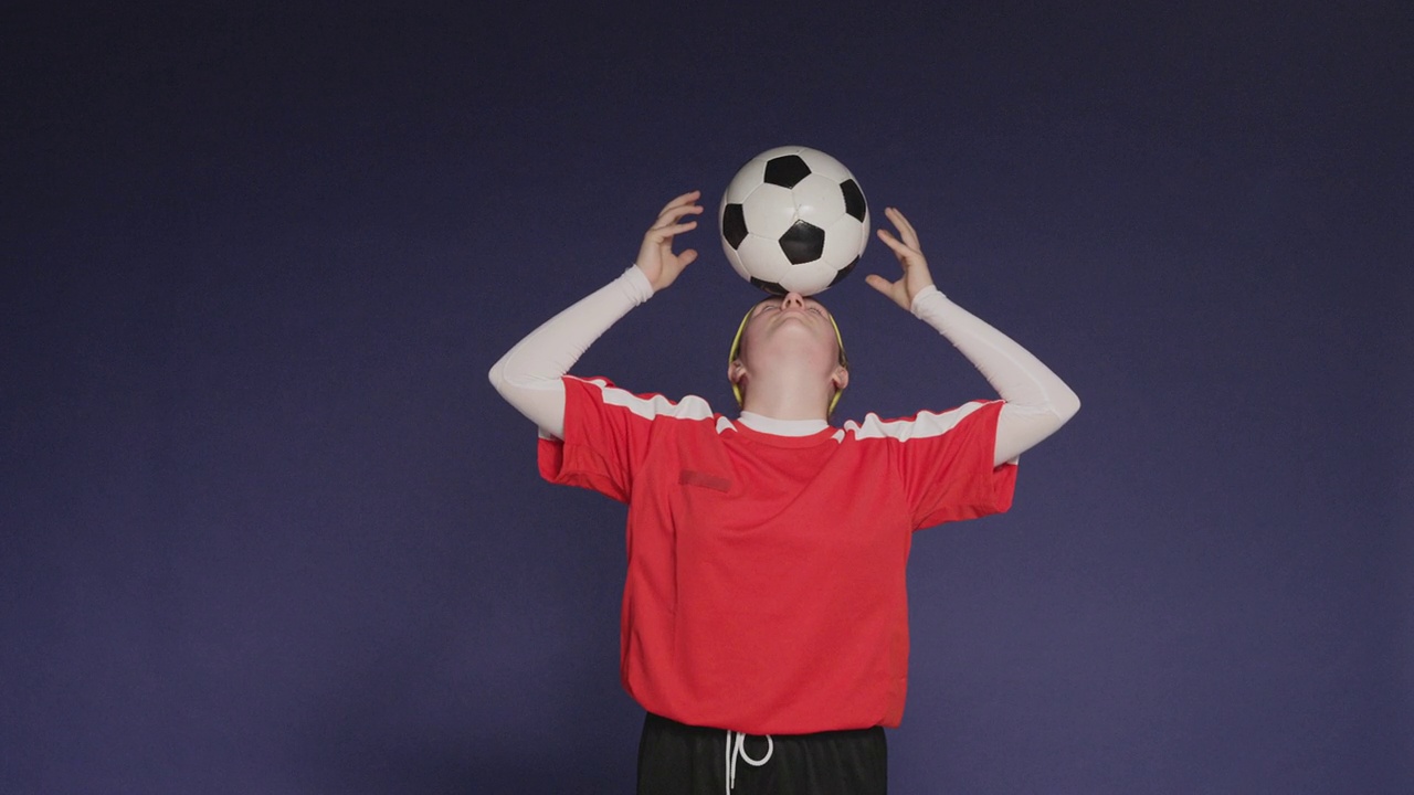 工作室拍摄了一个十几岁的女孩用前额平衡足球的镜头视频下载