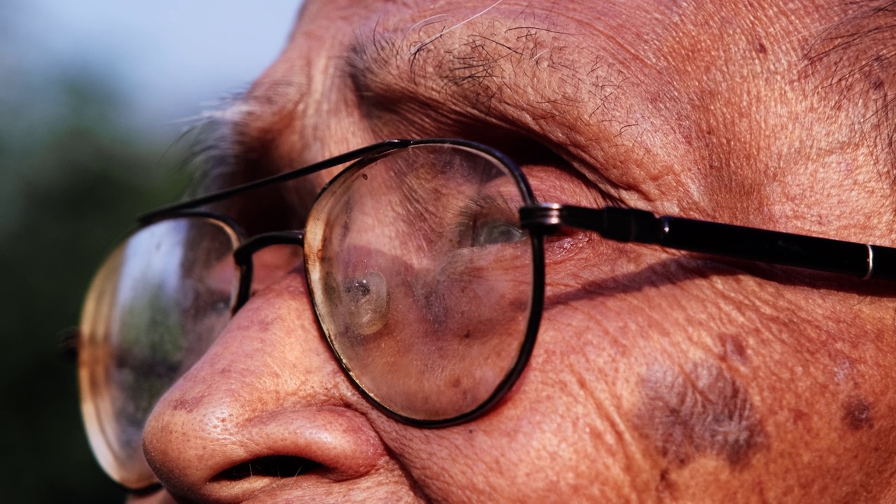 一位戴着眼镜的老人的特写脸，在阳光下眺望远方。眼光和老年人的观念视频下载