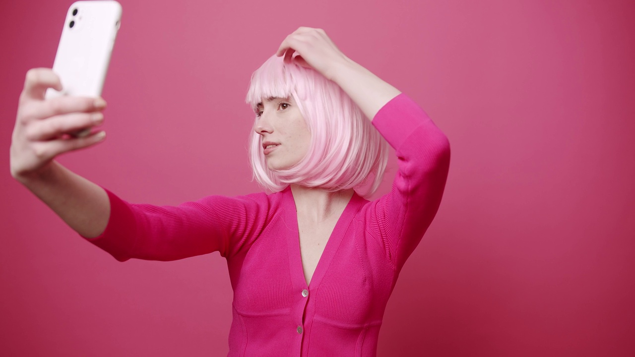 年轻漂亮的女人与粉红色的头发拍照，自我孤立的粉红色背景视频下载