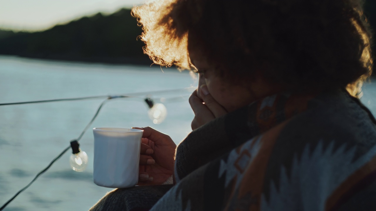 日落时分，一名年轻女子在一艘帆船的甲板上喝茶时打了个喷嚏视频素材