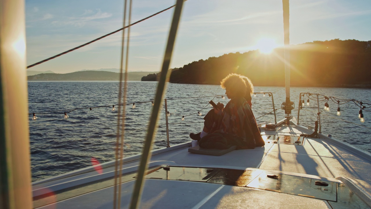 日出时分，两个年轻女子坐在一艘帆船的甲板上视频素材