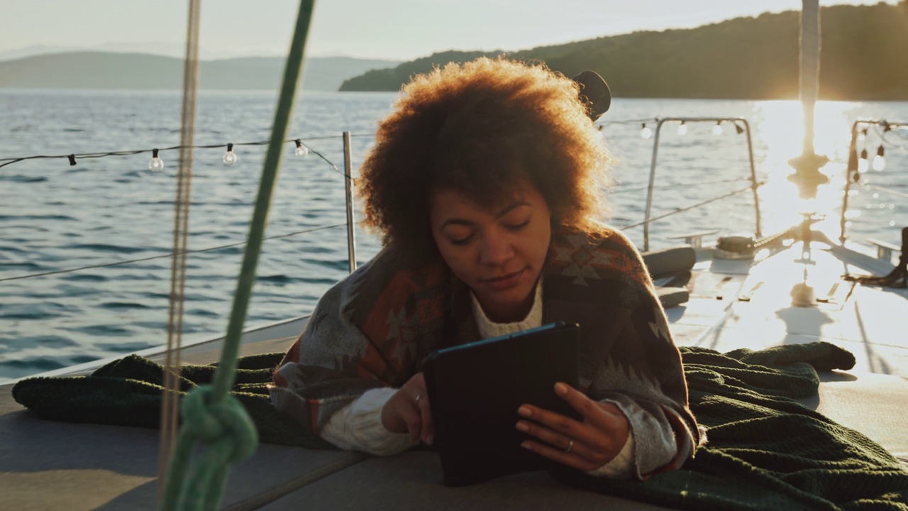 日出时分，一名年轻女子在一艘帆船的甲板上使用数码平板电脑视频素材