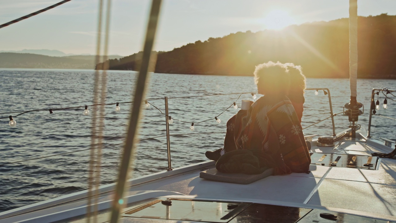 日出时分，两名年轻女子在一艘帆船的甲板上喝视频素材