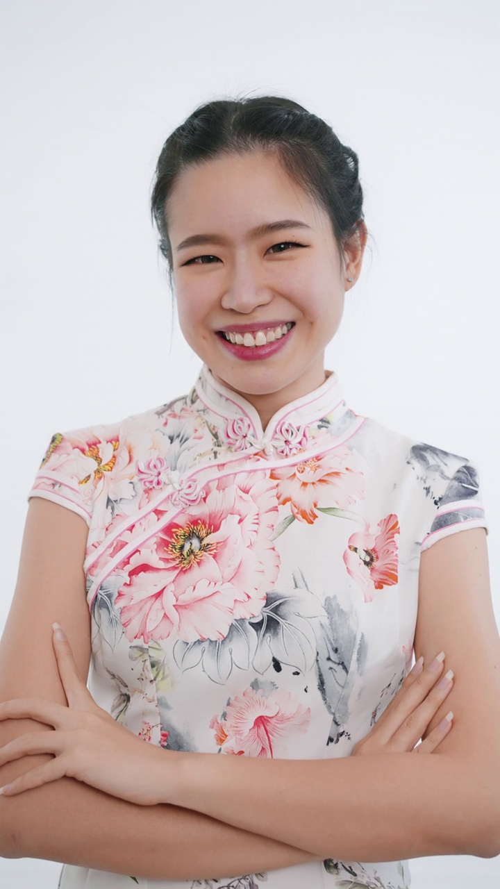 中国/亚洲妇女站在微笑，交叉手臂，看着镜头在中国春节期间，白色背景，穿着旗袍白色花卉图案的服装视频下载