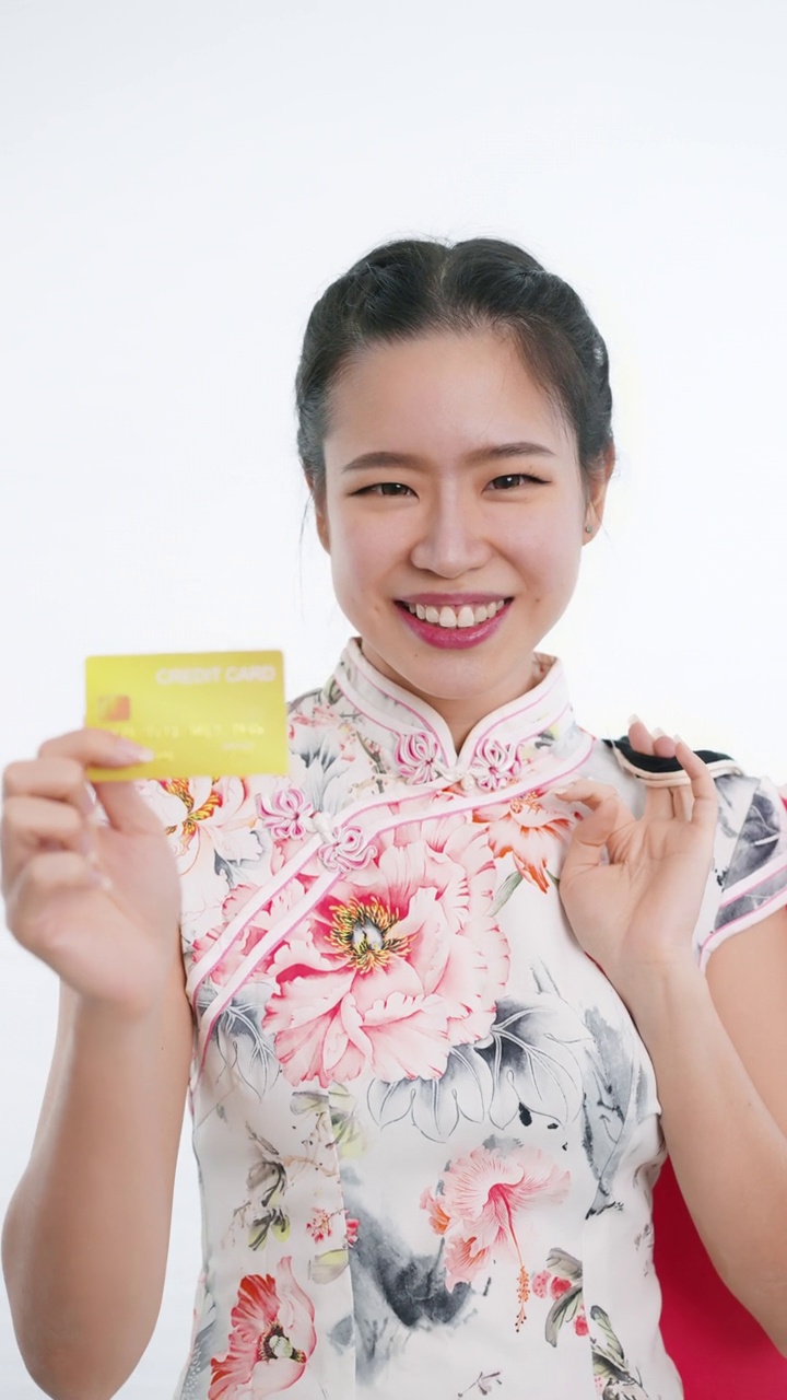 中国/亚洲妇女穿着旗袍白色花卉服装，在春节期间，拿着购物袋在白色的背景下用信用卡购物视频下载