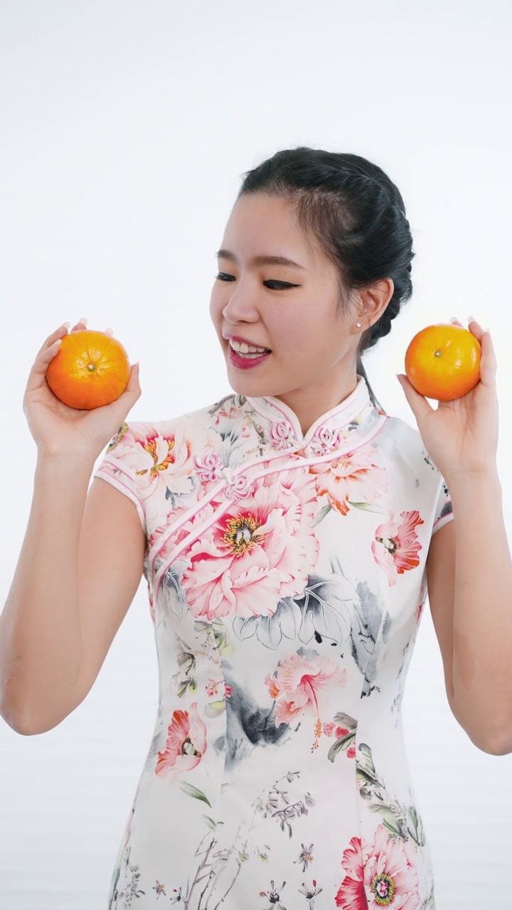 中国/亚洲妇女身穿旗袍，手拿橘子送给家人、亲戚和朋友，表示新年快乐、富裕、幸福和幸运视频下载