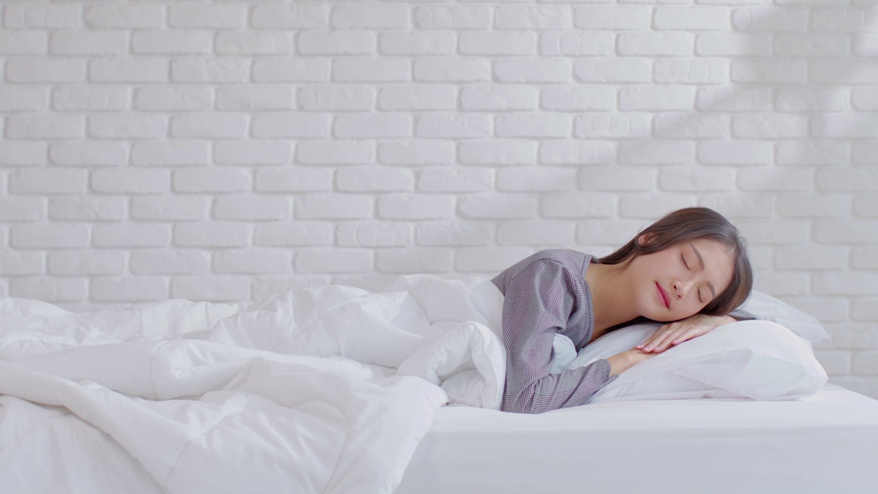 美丽迷人的亚洲女人睡觉和甜蜜的梦躺在床上舒适的卧室早上感觉如此放松和舒适。健康年轻女性在家就寝。医疗保健的概念视频购买
